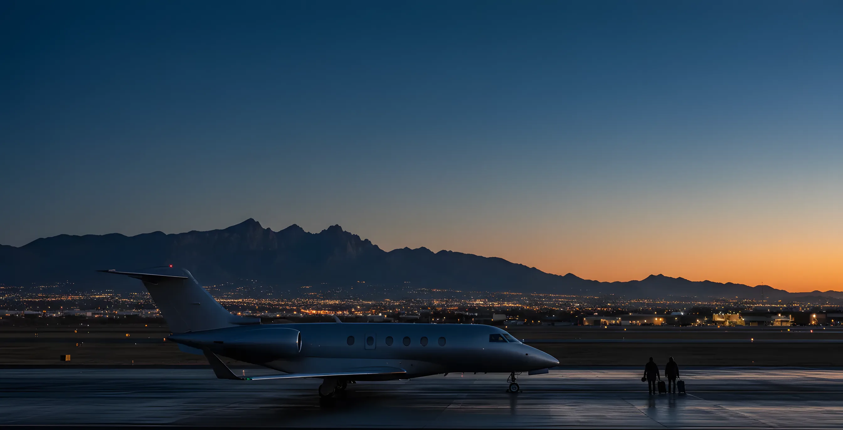 A private jet on an airport tarmac at dusk, with mountains and the glowing lights of Tucson, Arizona in the background.