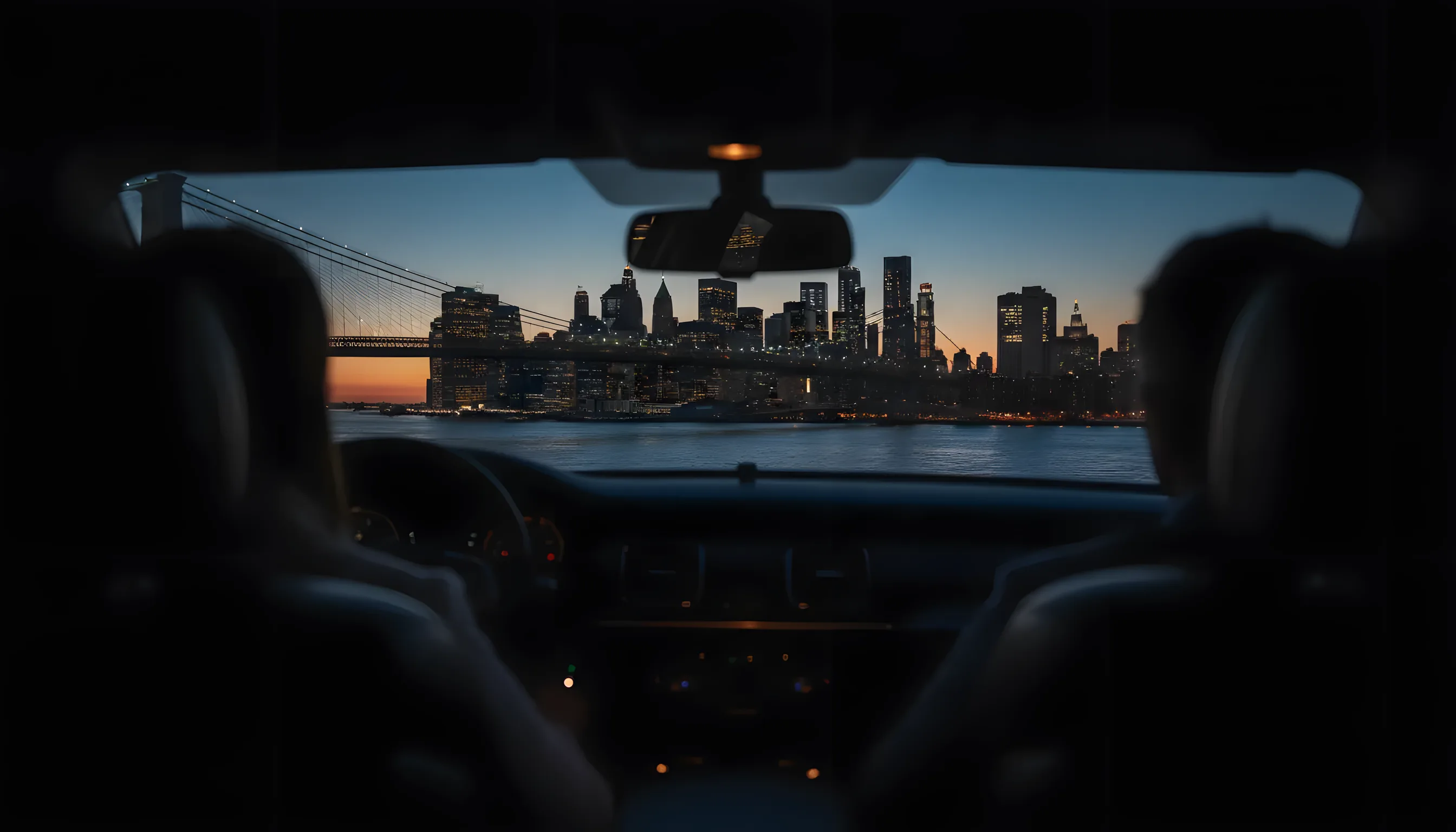 View of the Manhattan skyline at dusk from the backseat of a car on a bridge.