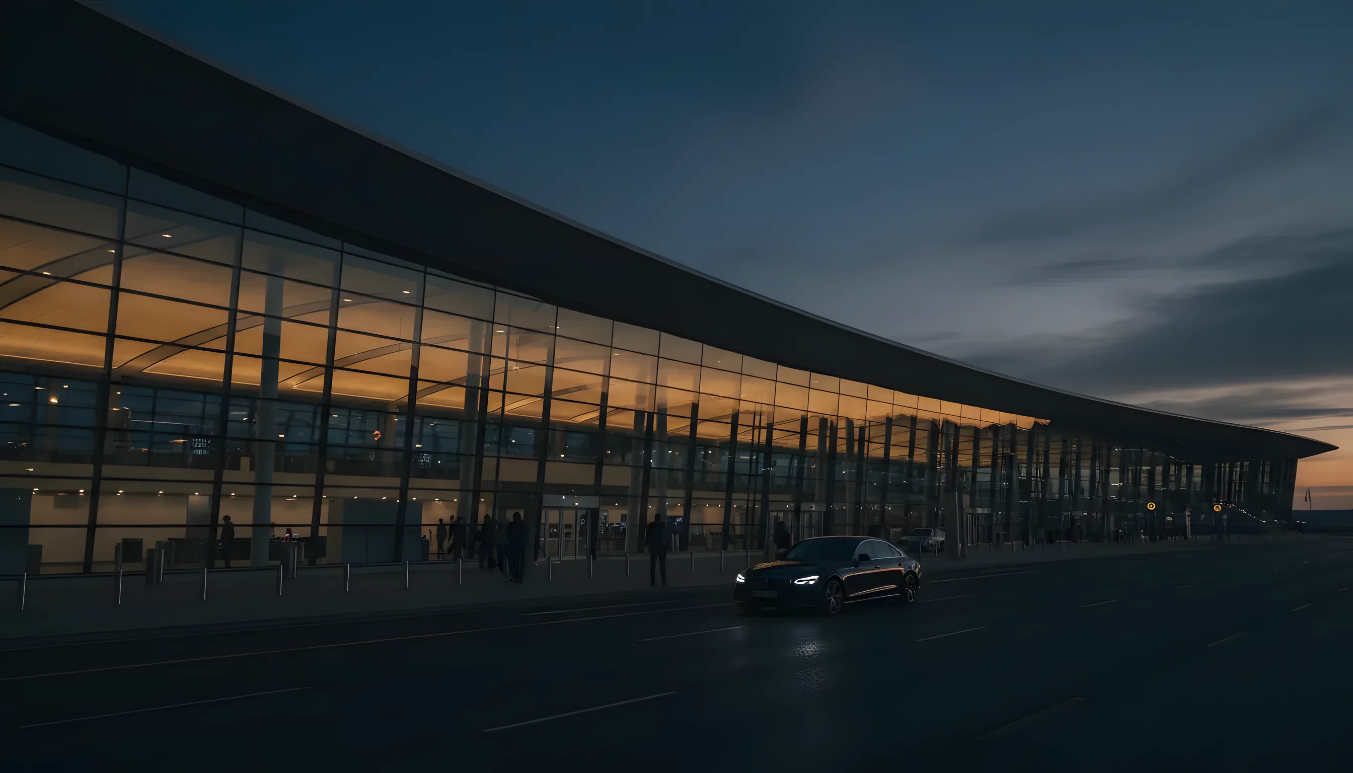 A modern glass airport terminal at dusk, its interior lights glowing warmly as a car arrives at the curb.