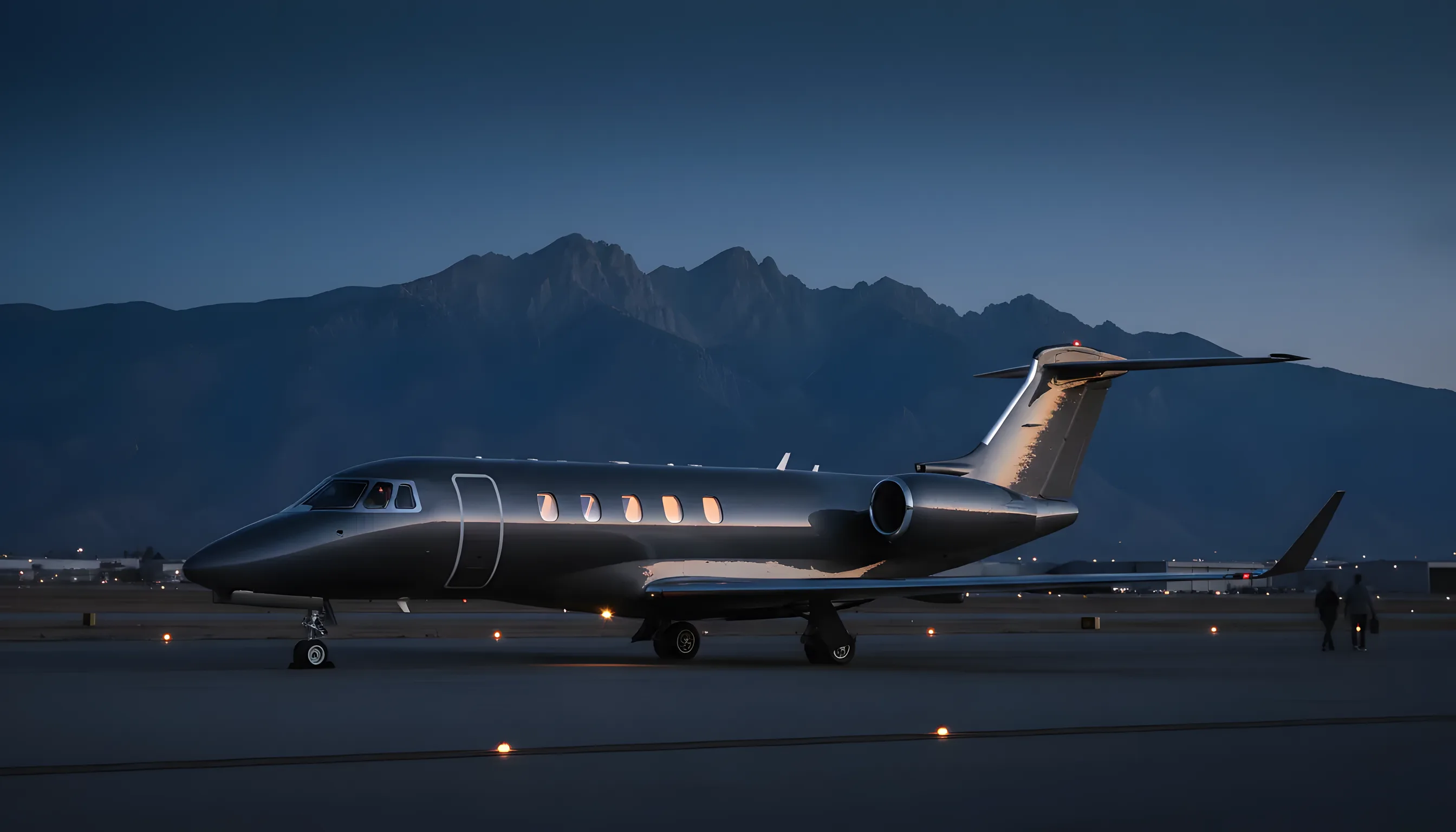 A private jet on an airport runway at dusk, with mountains in the background.