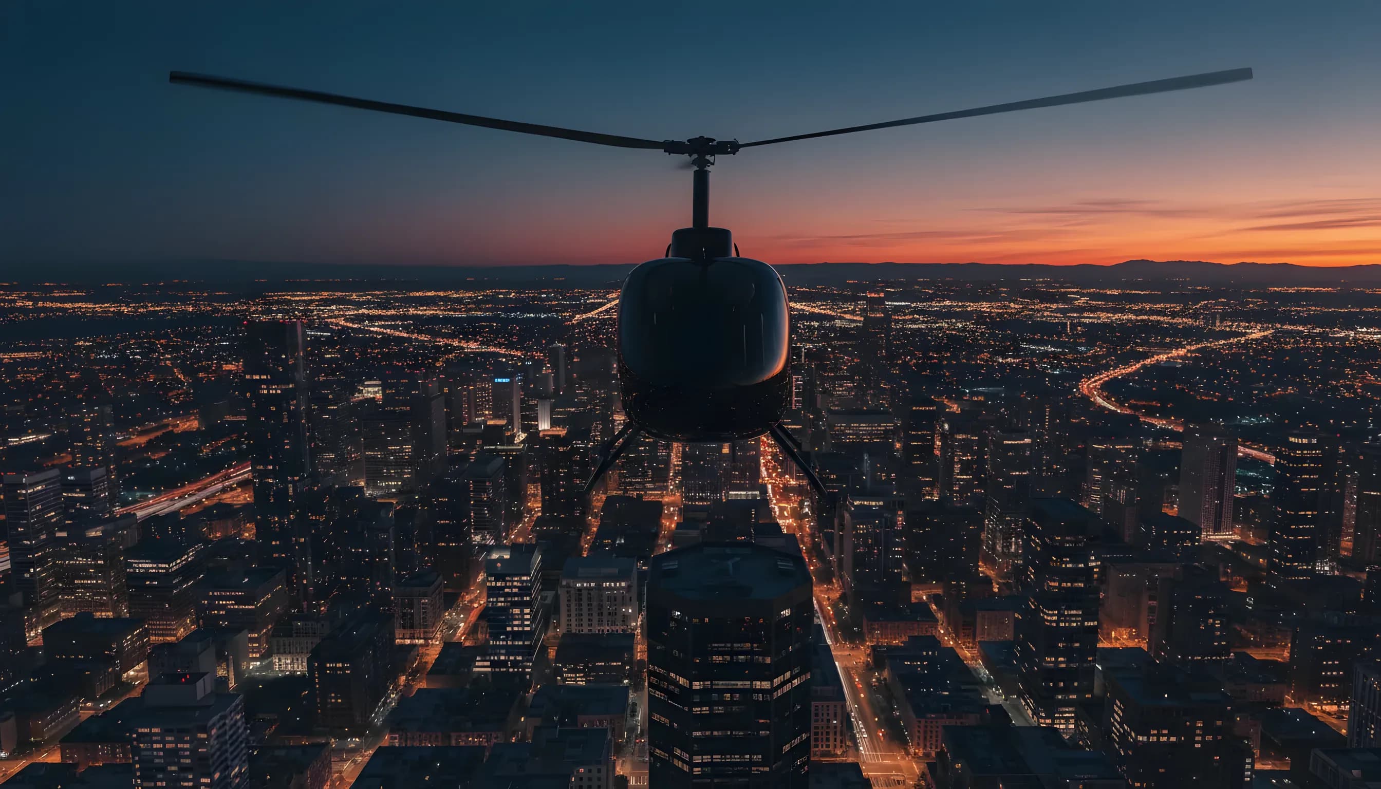 A helicopter flies over a brightly lit city grid at dusk.