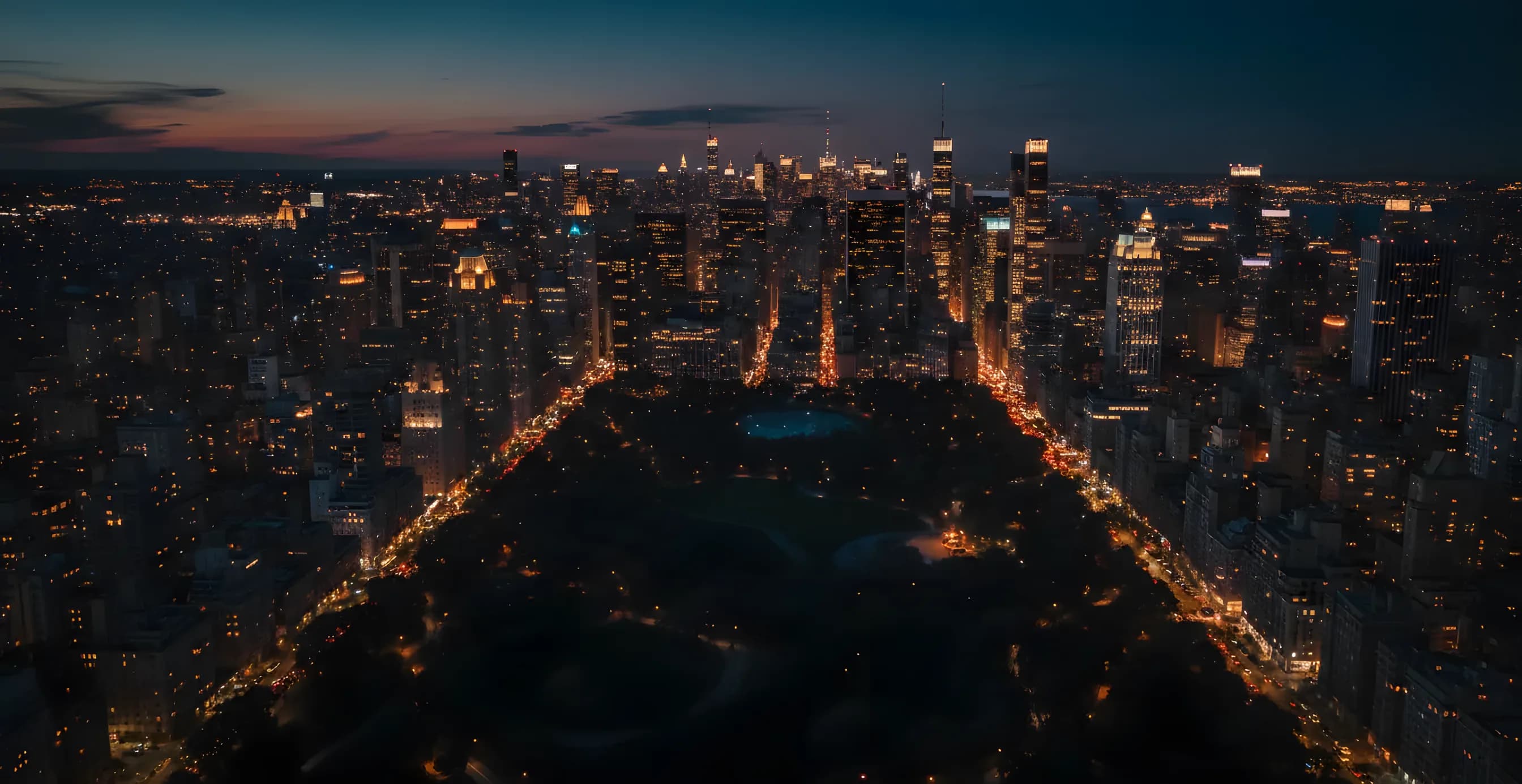 Aerial view of the Manhattan skyline at dusk, with city lights glowing against a dark blue sky.